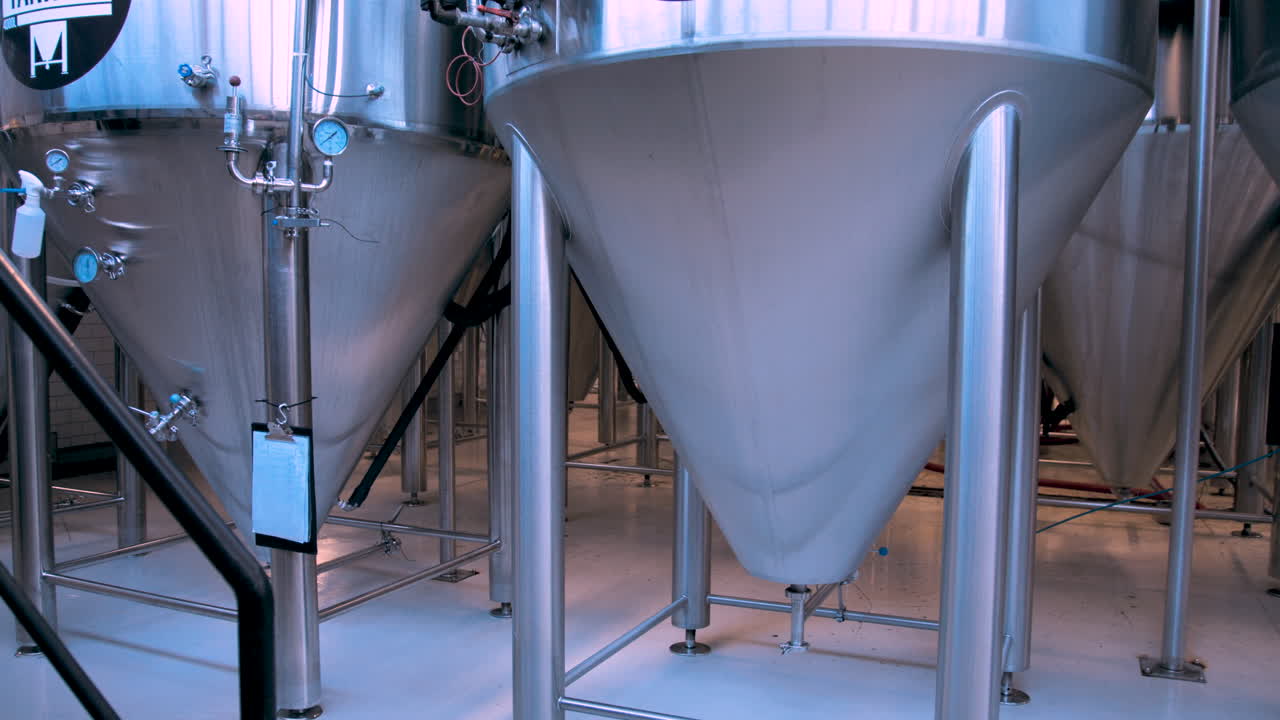 Slow pan left of large stainless steel beer fermentation tanks in a brewery