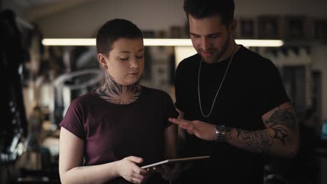 dos personas caucásicas con tatuajes discutiendo sobre un nuevo proyecto.