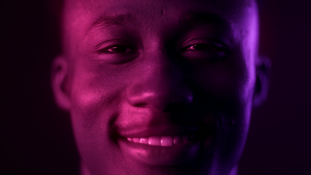 Close-up portrait of a smiling man with vibrant purple and pink lighting