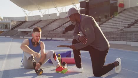 Diverse-male-coach-and-disabled-athlete-with-prosthetic-leg-talking-during-training-session