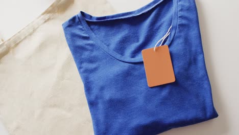 video of close up of folded blue t shirt with tag on white background