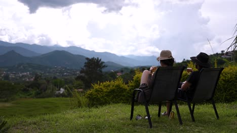 Man-and-woman-enjoy-the-sunset-in-a-beautiful-mountain-landscape,-while-eating-and-drinking