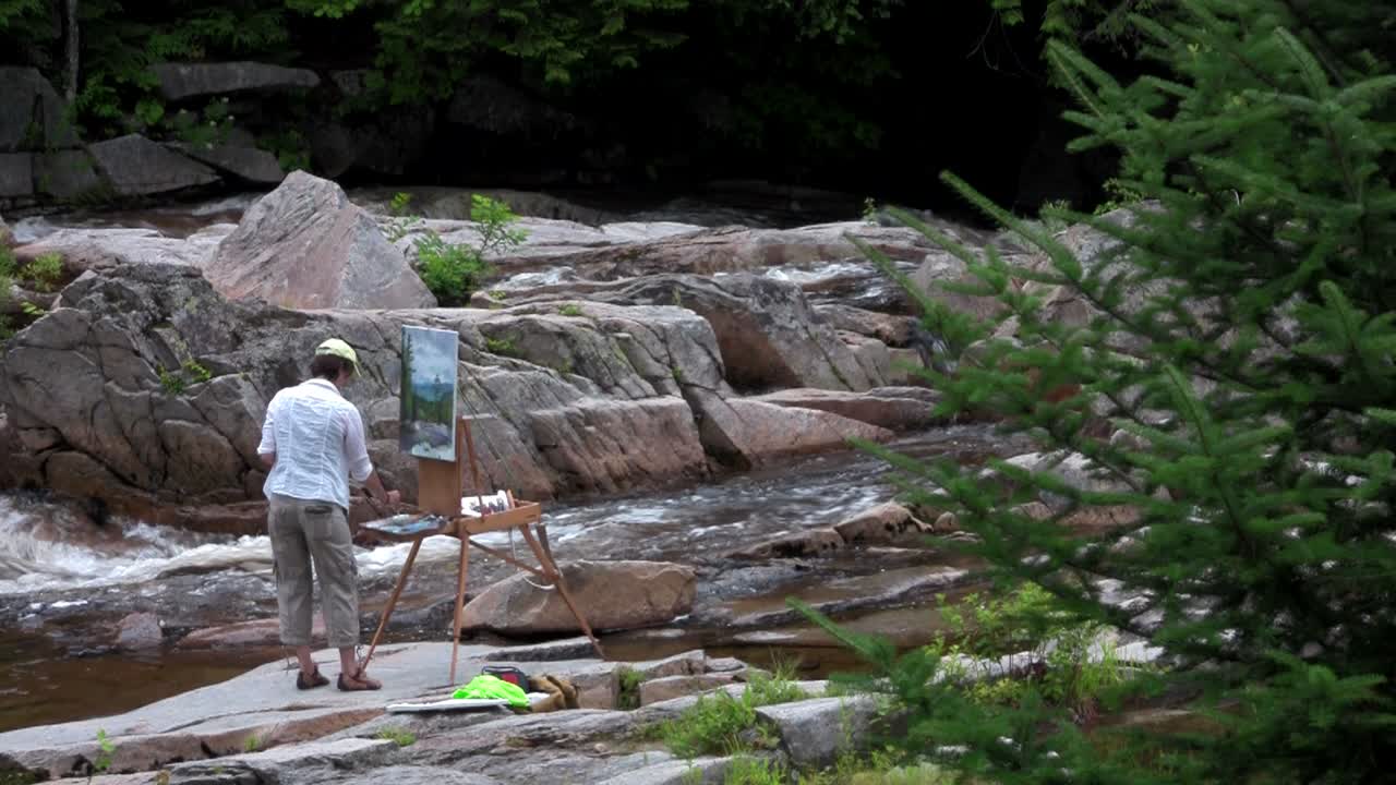 예술가는 자연의 강 옆에 그림을 그립니다.