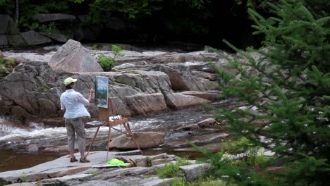 Un-Artista-Pinta-Un-Cuadro-Junto-A-Un-Río-En-La-Naturaleza