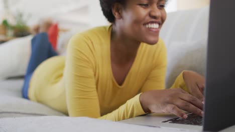 Glückliche-Afroamerikanische-Frau,-Die-Mit-Laptop-Auf-Dem-Sofa-Liegt
