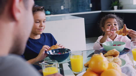 padre hispano con niños sentados alrededor de la mesa comiendo el desayuno juntos