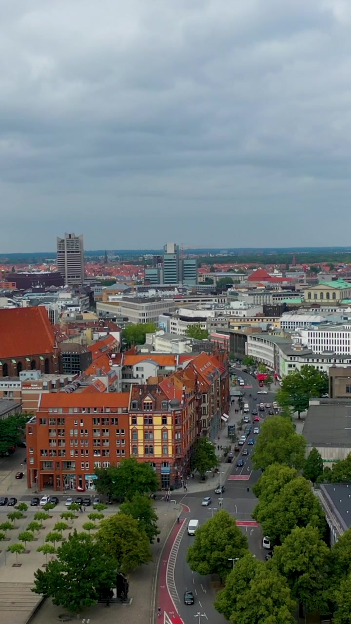 En filmisk vertikal droneoptagelse, der svæver op over Hannovers gader i Tyskland, og viser bytrafik, røde cykelstier og historisk arkitektur.