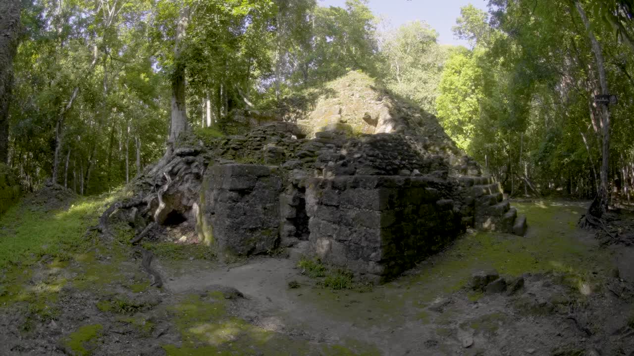View of ancient Maya structures at La Muerta, a hidden archaeological site in the jungle of El Petén, Guatemala. The ruins are partially covered by forest, evoking mystery and lost civilization.