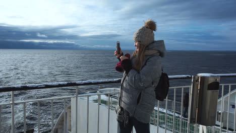 young woman taking photos of the sea from a ferry deck in winter