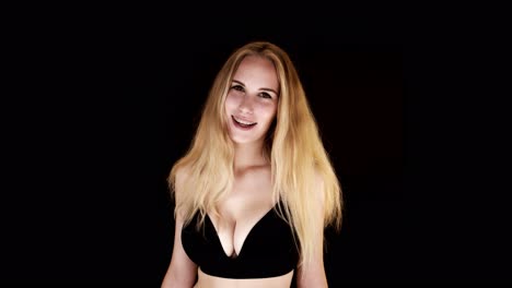 beautiful young woman with big natural breasts in a black bra on a black background laughing at the camera