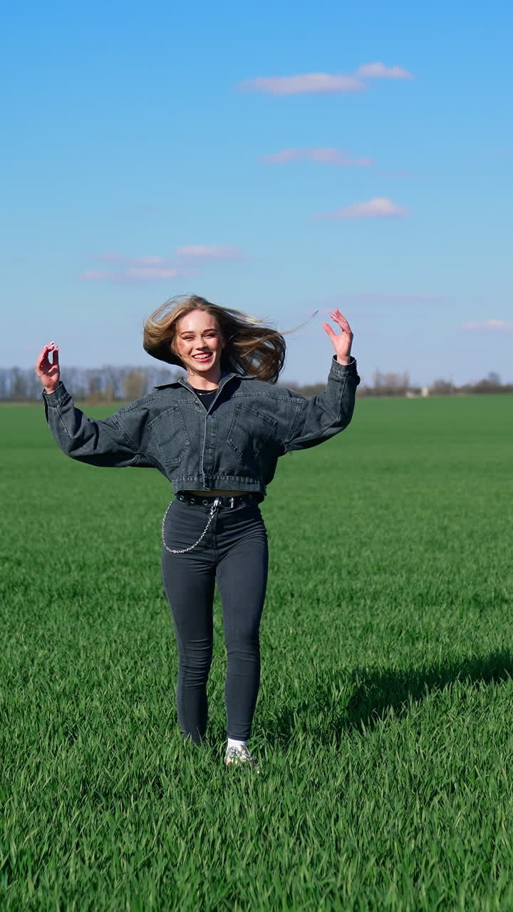 Joy girl on a green meadow. Beautiful young woman in denim costume enjoys nature in spring. Attractive female jumping on a meadow happily. Vertical video