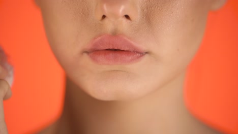 disparo de cerca de los labios de una mujer joven y llena mientras una mujer joven se limpia los labios después de comer con un pañuelo blanco contra un fondo naranja en cámara lenta