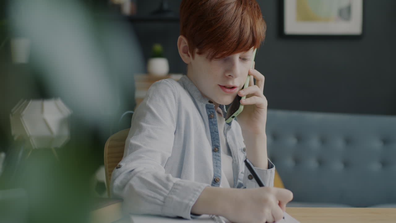 Teenage boy on a phone call while doing homework at home