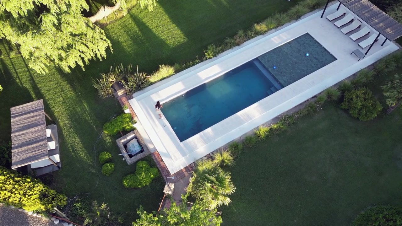 Aerial pulls in as woman tests swimming pool water in landscaped yard