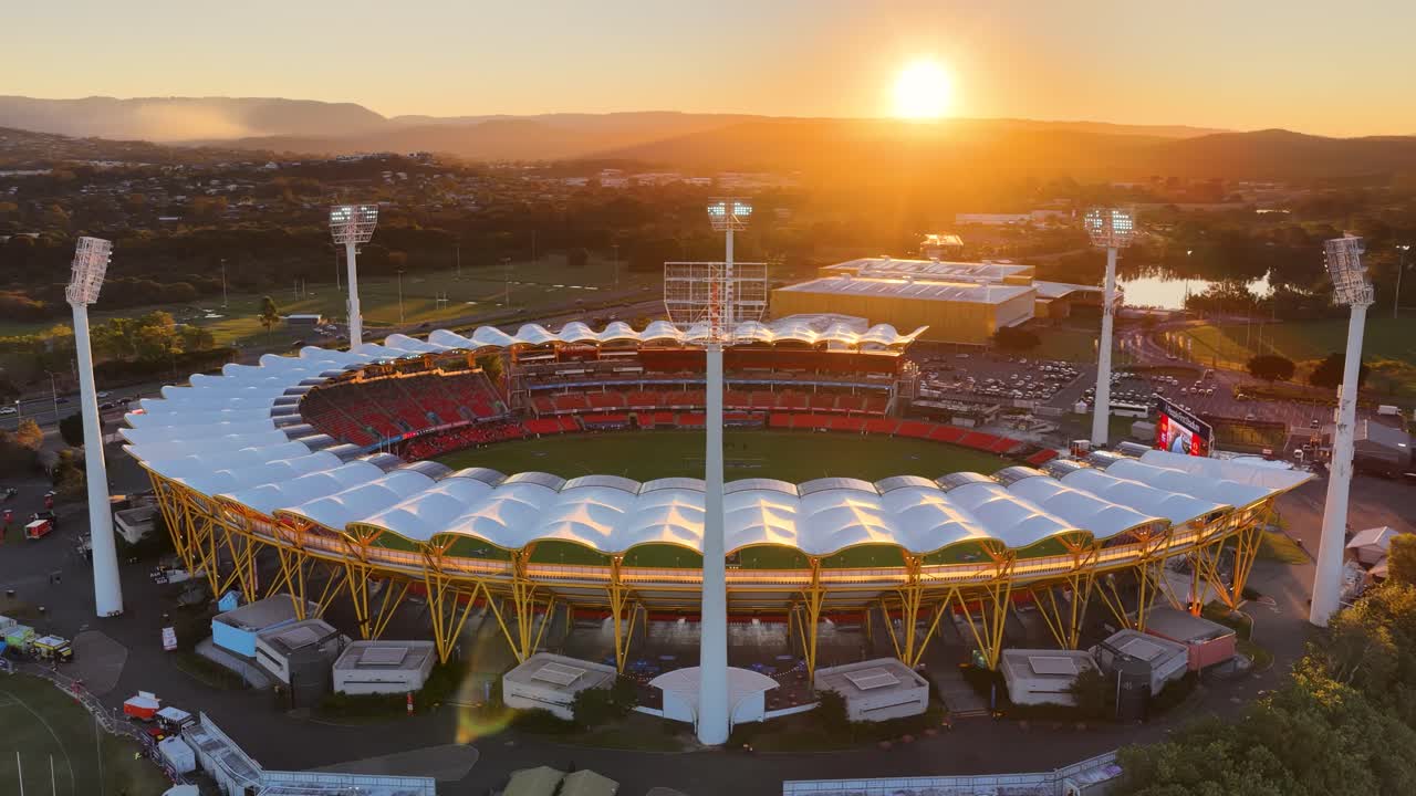 Drone footage circles a brightly lit stadium at sunset, highlighting architectural details, event lighting, and the nearby river in a vibrant urban landscape