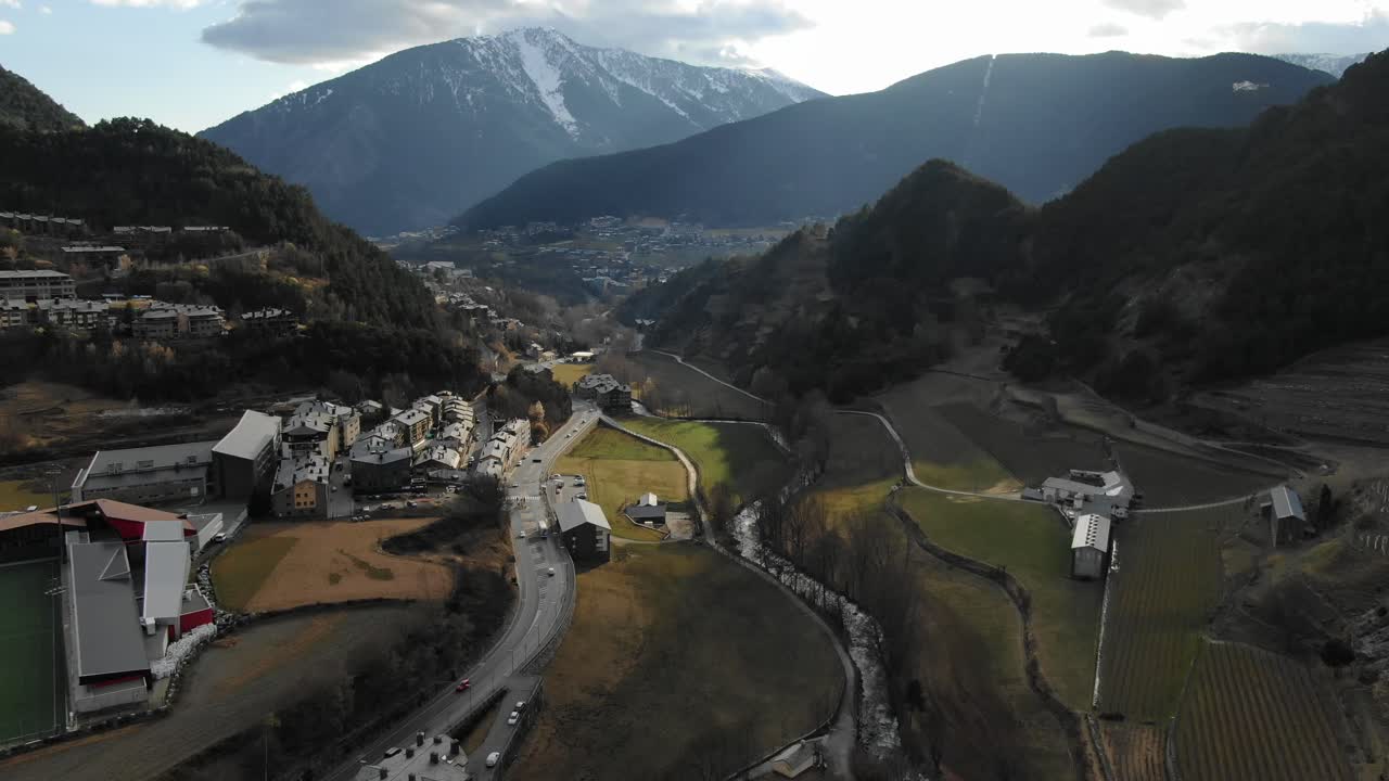 Aerial view of nestled Andorran town in valley with roads, river, and snow-capped mountains. Scenic European valley landscape, travel destination, Andorra
