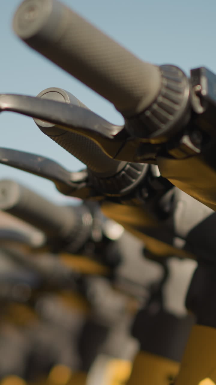 Primer plano de los detalles de la palanca de freno del manillar de un scooter, empuñaduras de goma texturizadas y juntas metálicas, poca profundidad de campo con bokeh suave, la luz del sol resalta las marcas de desgaste, se sugiere a un mecánico ajustando el freno