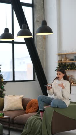 woman relaxing on sofa with phone during christmas celebration