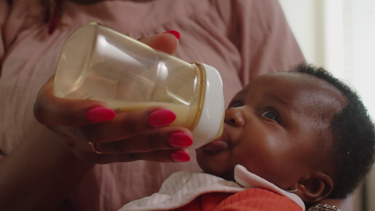 Newborn Girl Drinking from Baby Bottle in Hands of Mother
