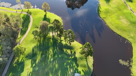 drone captures lush golf course landscape with winding river, vibrant greens, and long shadows in golden sunlight
