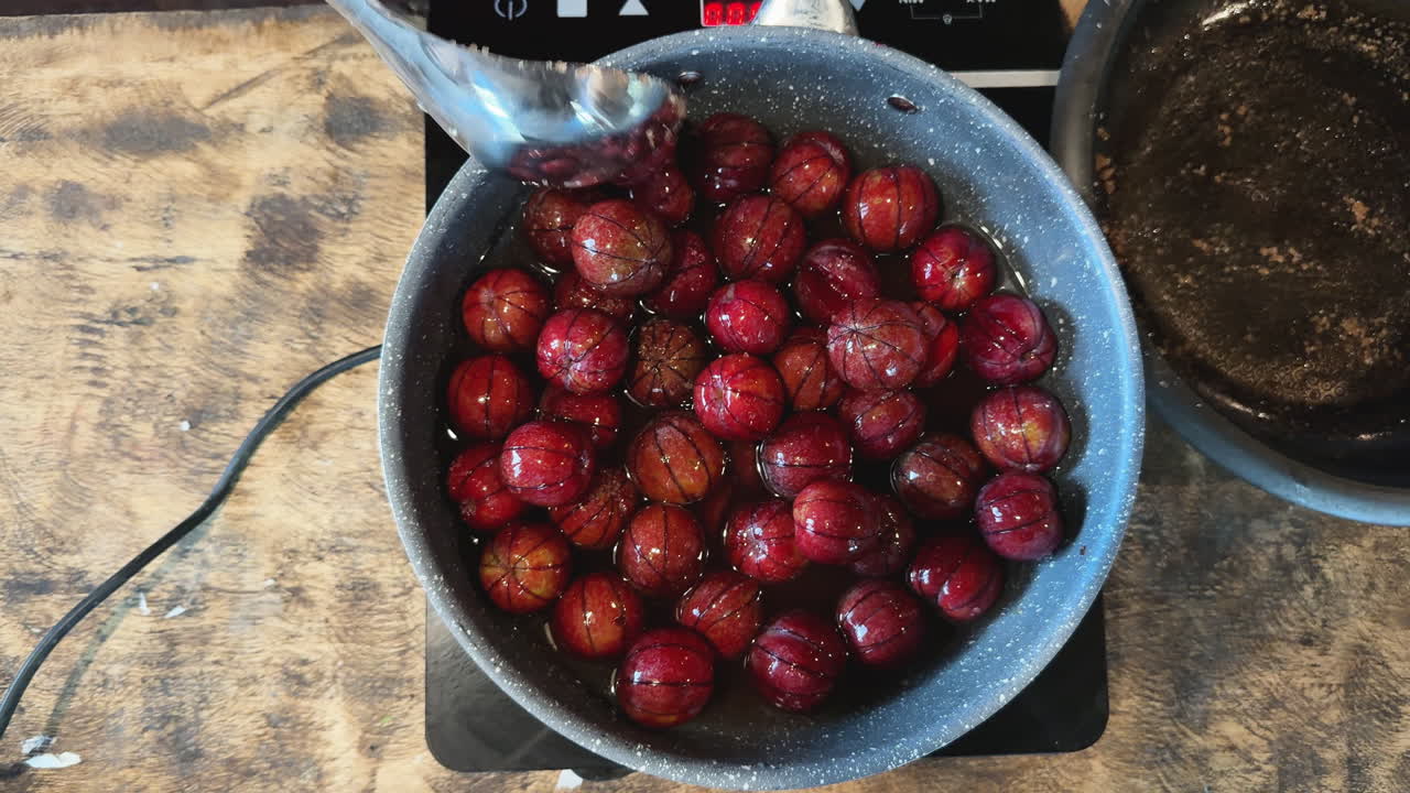 Overhead shot of ripe red plums boiling in pot with spoon stirring in sweet syrup