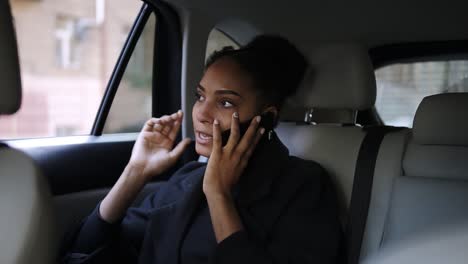 Beautiful-Afro-American-businesswoman-sitting-on-the-backseat-of-a-taxi-with-bright-leather-salon,-talking-by-her-mobile-phone.-Relaxed-woman-talking-by-phone-in-the-car.-Slow-motion