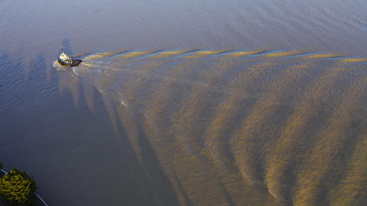수입 수출 계약을 위해 또 다른 보트를 바다로 끌어내기 위해 항구 부두로 돌아가는 황혼의 일몰 진흙탕 물에 파도를 일으키는 상업 강을 지나가는 공중 조감도 예인선