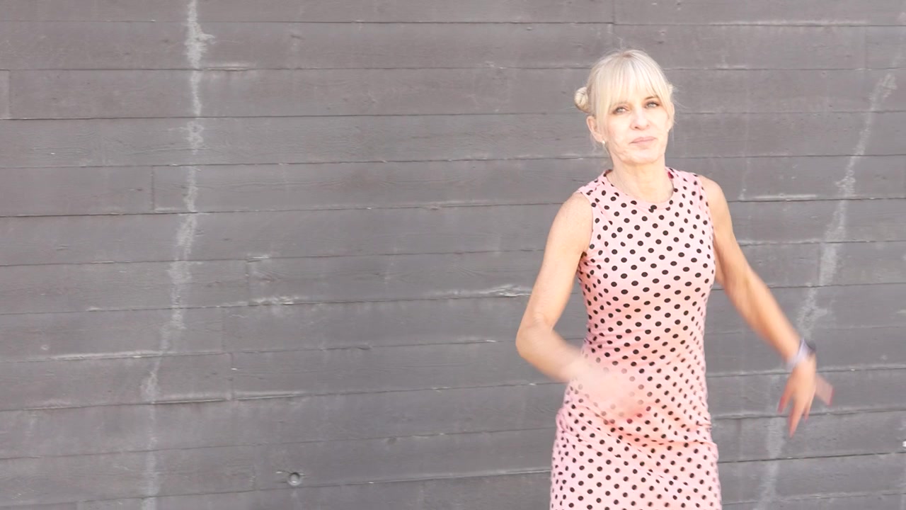 Una mujer elegante con un vestido rosa de lunares irradia elegancia y moda chic contra una pared gris.