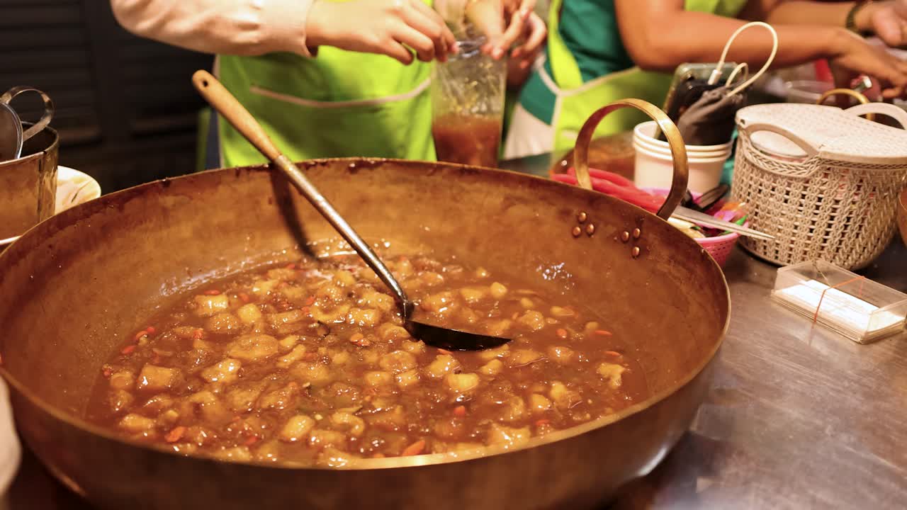 Vendor stirs large pot of fish maw soup at night market, warm lighting, handheld camera
