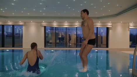 hombre y mujer saltando a la piscina cubierta