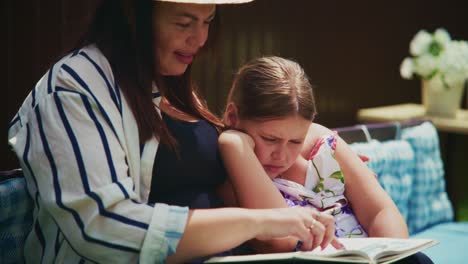woman reading a storybook to a young girl on a cozy sofa in a warm, inviting setting