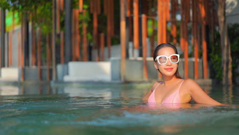 Attractive-asian-woman-on-tropical-vacation-enjoying-in-swimming-pool-on-a-sunny-day