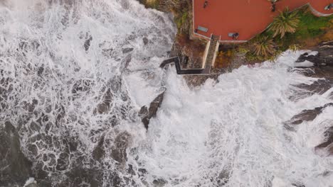 nervi coastline in genoa, italy, with waves crashing against rocks, a walkway visible, aerial view