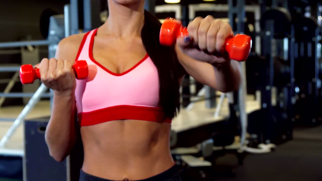 The sports girl does special exercises for hands with two dumbbells