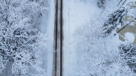 top to down view of drone flying forward following the frozen road in the winter forest