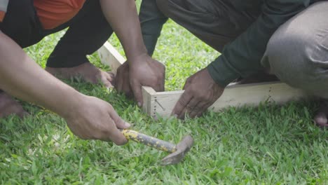 dos hombres golpeando clavos con martillos en la madera