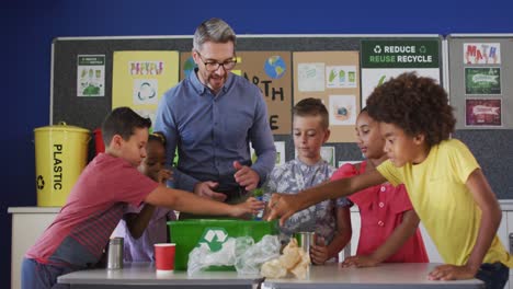 Diverse-teacher-and-schoolchildren-standing-in-classroom-learning-about-recycling-trash