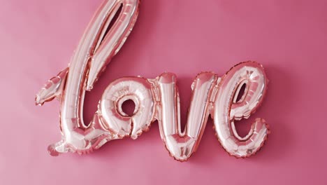 overhead video of shiny pale pink love text balloon, on pink background with copy space