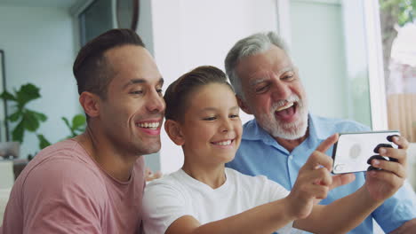 familia hispana masculina de varias generaciones en el sofá en casa posando para una selfie en el teléfono móvil
