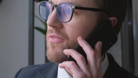 Man in Suit with Tie and Glasses Talking on Cell in Office. In the video, a man in a suit and tie is talking on a cell phone. He wears glasses and seems focused on a serious conversation. The surroundings indicate a business or office setting