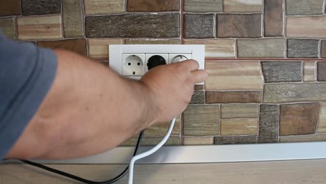 Wide-frame-of-triple-power-wall-socket-being-plugged-and-unplugged-with-devices,-by-a-man's-hand