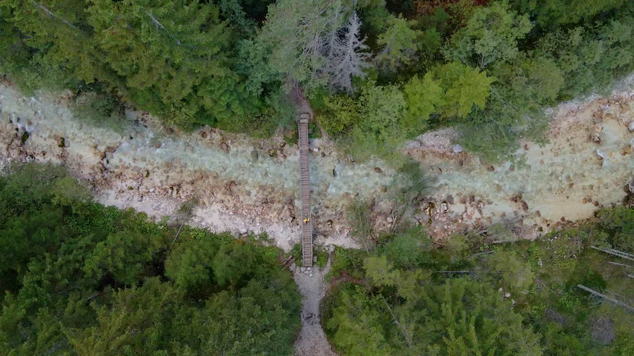 Aerial capture of a man walking across bridge over river amid trees, Triglav, Slovenia