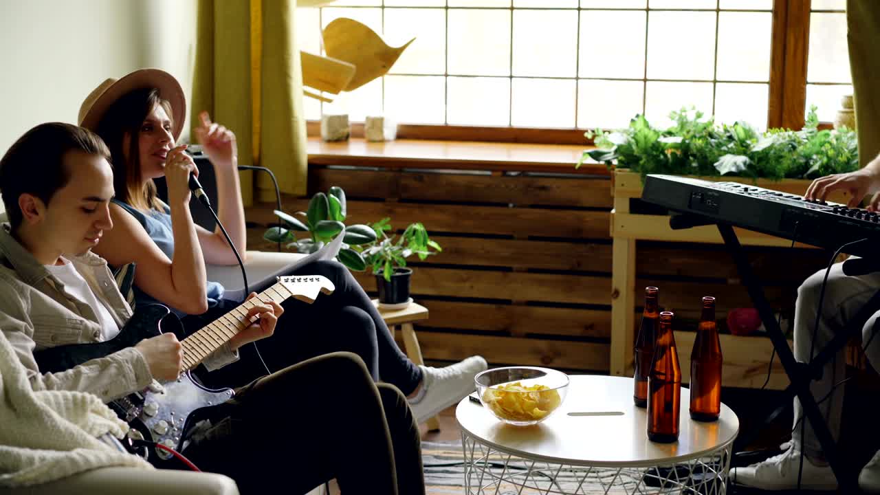 아마추어 음악 그룹은 집에서 공연을 연습하고, 여성 보컬은 마이크에서 노래하고, 소년들은 악기를 연주하고 있습니다.