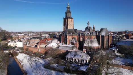 ascending aerial movement with the walburgiskerk cathedral of medieval hanseatic dutch tower town zutphen in the netherlands covered in snow rising above historic heritage cityscape