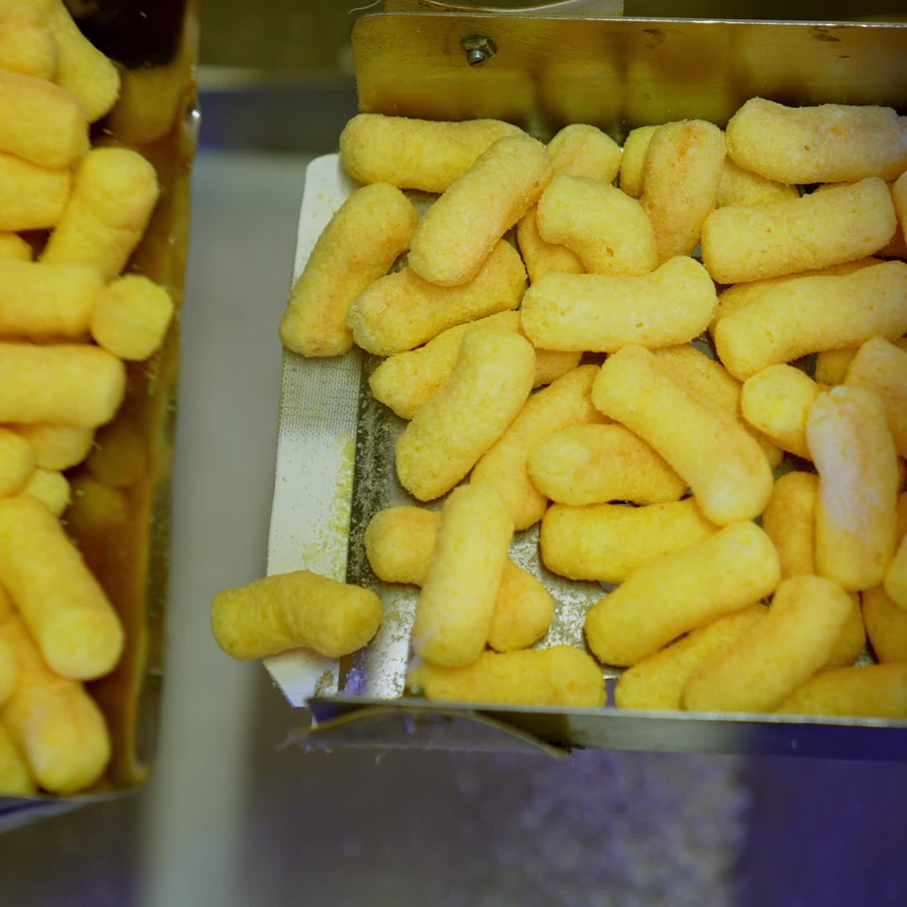 Metal boxes at conveyor belt being filled with sweet snacks. Production on maize crispy sticks at modern food plant. Close up