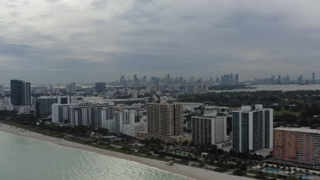 video aéreo moviéndose rápidamente más allá de los edificios a lo largo de la costa del norte de la playa de miami con el centro de miami en el fondo