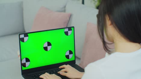 mujer étnica de raza mixta acostada en el sofá en casa, usa una computadora portátil con pantalla de maqueta verde. sobre el hombro de la mujer en la sala de estar.