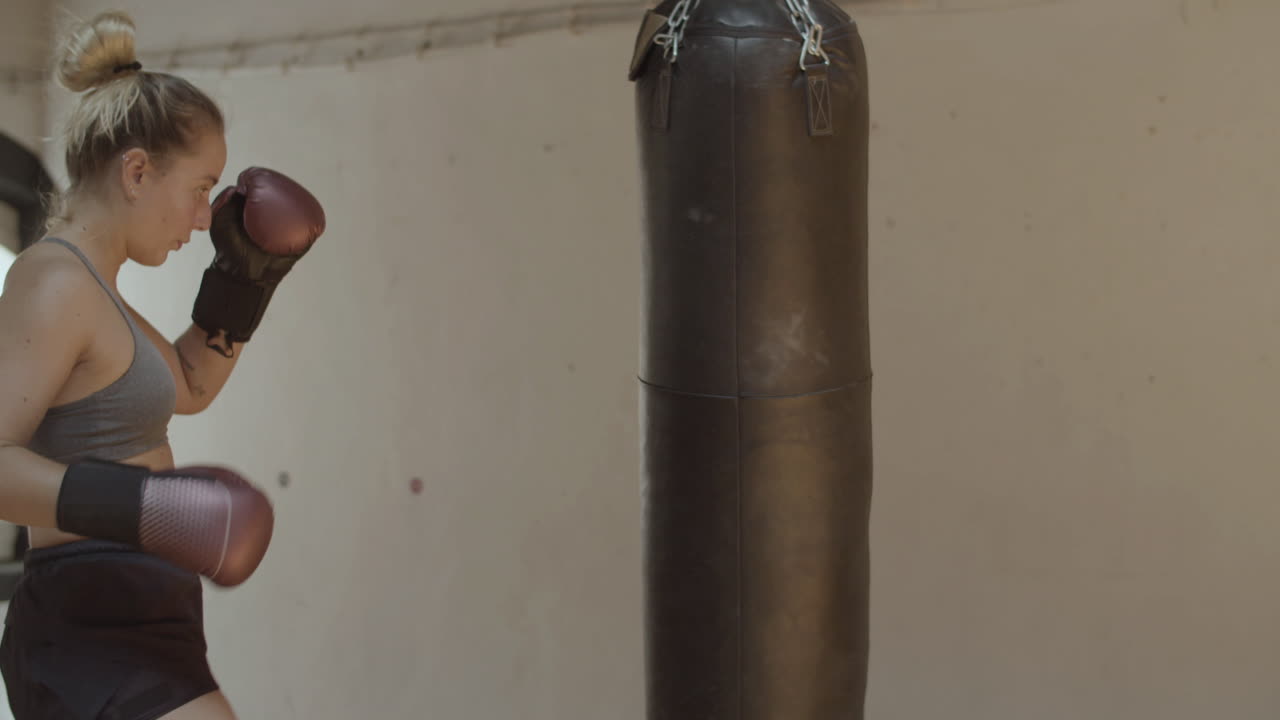Di profilo, donna energica che sferra pugni e calci a un sacco da boxe