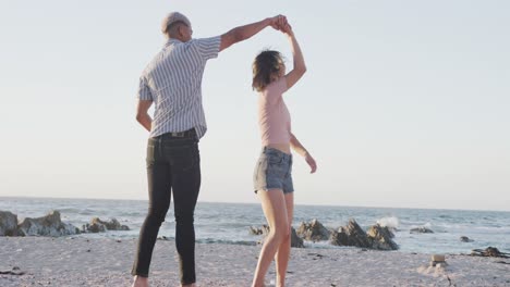 Happy-biracial-couple-dancing-together-at-beach,-in-slow-motion