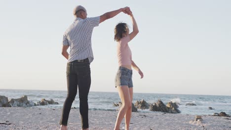 happy biracial couple dancing together at beach, in slow motion